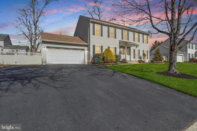 colonial home with driveway, a yard, an attached garage, and fence