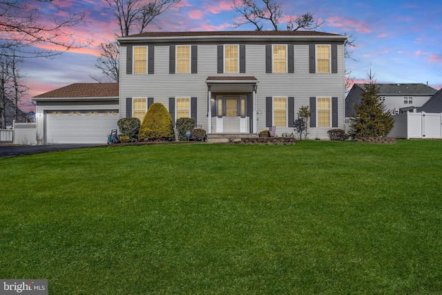 colonial inspired home with aphalt driveway, a front yard, fence, and an attached garage