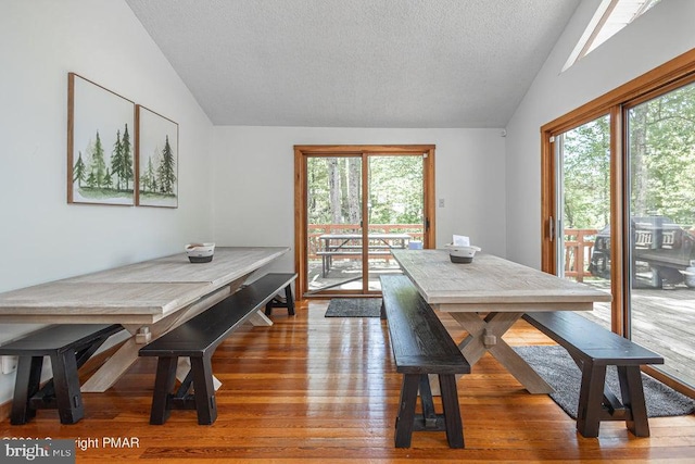 dining space featuring a healthy amount of sunlight, vaulted ceiling, a textured ceiling, and wood finished floors