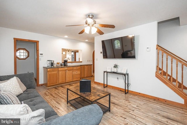 living room featuring light wood finished floors, baseboards, and stairway