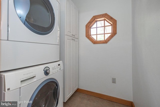 laundry room with stacked washer / dryer, tile patterned flooring, cabinet space, and baseboards