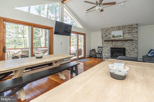 living area featuring wood-type flooring, ceiling fan, a stone fireplace, high vaulted ceiling, and beam ceiling