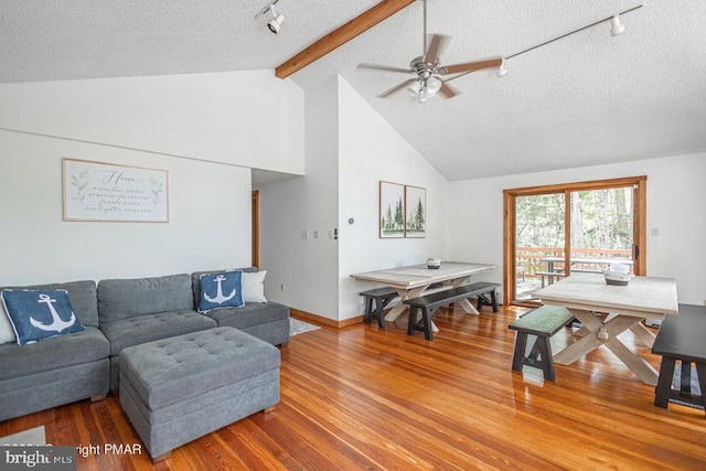 living area featuring a textured ceiling, wood finished floors, a ceiling fan, beamed ceiling, and rail lighting