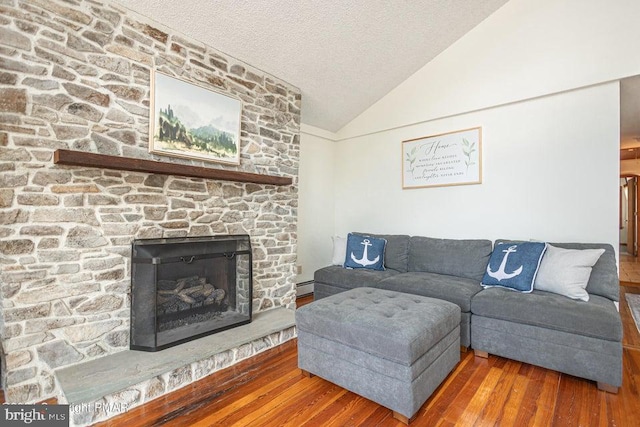 living room featuring a baseboard radiator, wood finished floors, vaulted ceiling, a textured ceiling, and a stone fireplace