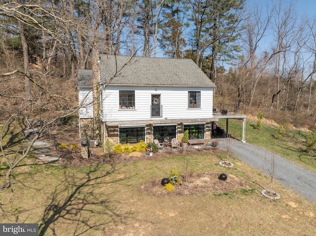 view of front facade with a front lawn, an attached carport, roof with shingles, and driveway