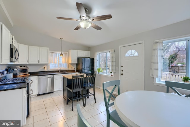 kitchen featuring dark countertops, stainless steel appliances, a healthy amount of sunlight, white cabinetry, and light tile patterned flooring