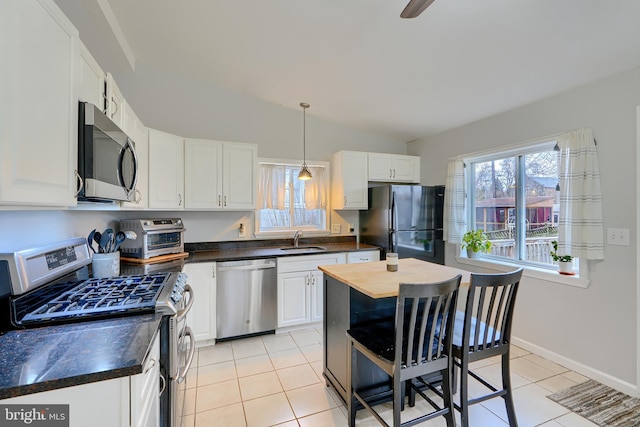 kitchen with light tile patterned floors, vaulted ceiling, stainless steel appliances, white cabinetry, and a sink