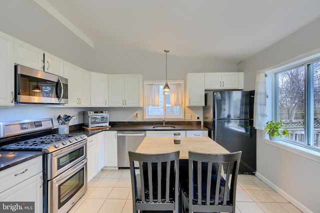 kitchen featuring light tile patterned floors, stainless steel appliances, dark countertops, lofted ceiling, and a sink