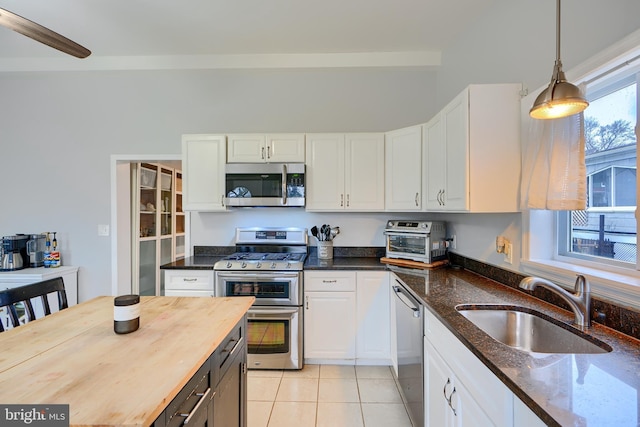 kitchen with appliances with stainless steel finishes, light tile patterned flooring, a sink, white cabinetry, and butcher block countertops