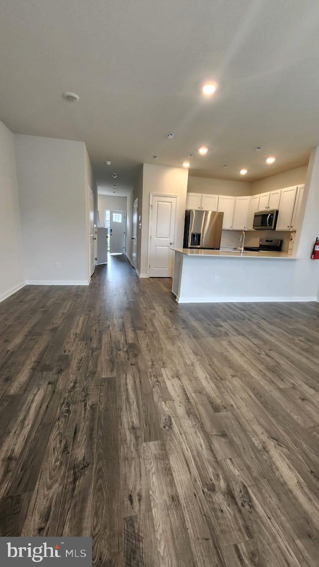 unfurnished living room with dark wood-style floors, recessed lighting, a sink, and baseboards