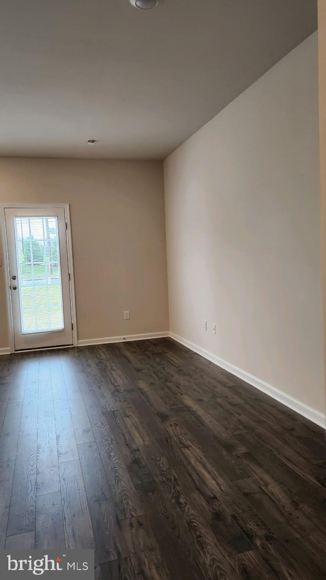 empty room with baseboards and dark wood-type flooring