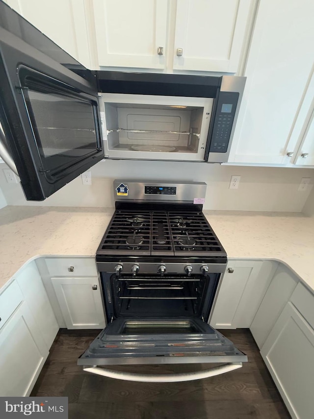 room details featuring light stone countertops, gas range, white cabinets, and dark wood-style flooring