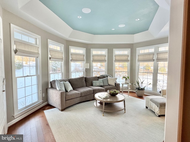 living room with wood-type flooring, a tray ceiling, baseboards, and recessed lighting