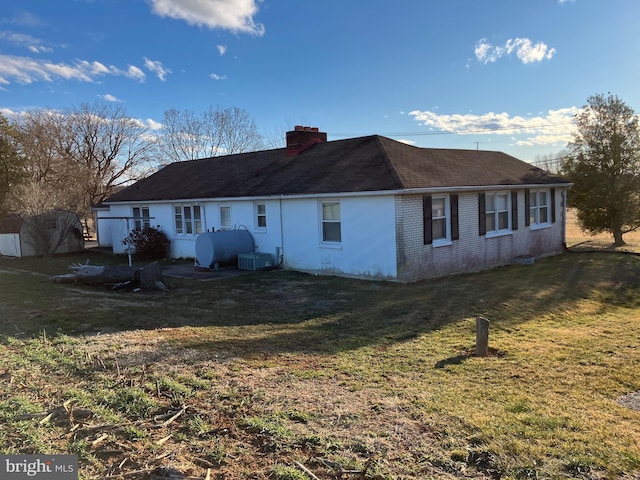 back of house with heating fuel, a yard, a chimney, and brick siding