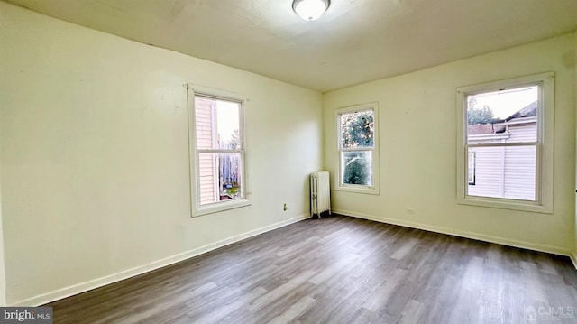 empty room featuring a wealth of natural light, baseboards, radiator, and dark wood-style floors