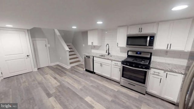 kitchen with tasteful backsplash, light wood-style flooring, stainless steel appliances, white cabinetry, and a sink