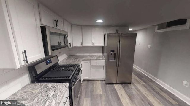 kitchen with appliances with stainless steel finishes, backsplash, light stone countertops, and white cabinets