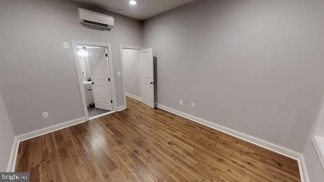 unfurnished room with an AC wall unit, baseboards, and wood finished floors