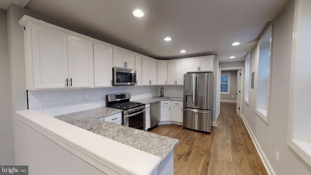 kitchen featuring white cabinets, decorative backsplash, appliances with stainless steel finishes, a peninsula, and light stone countertops