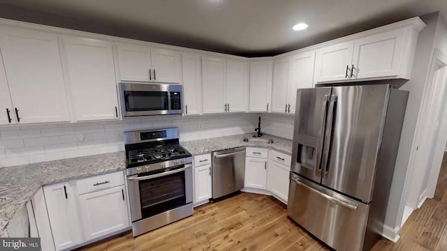 kitchen with stainless steel appliances, decorative backsplash, white cabinets, light stone countertops, and light wood-type flooring