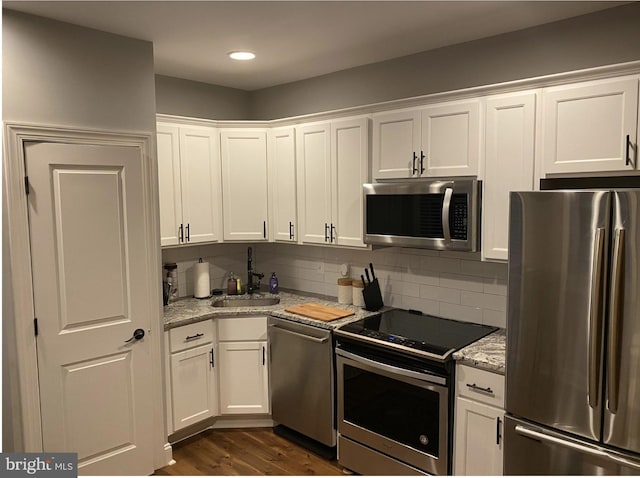 kitchen featuring dark wood-style floors, tasteful backsplash, appliances with stainless steel finishes, white cabinets, and a sink