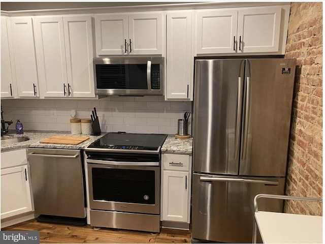 kitchen with brick wall, appliances with stainless steel finishes, wood finished floors, and white cabinetry