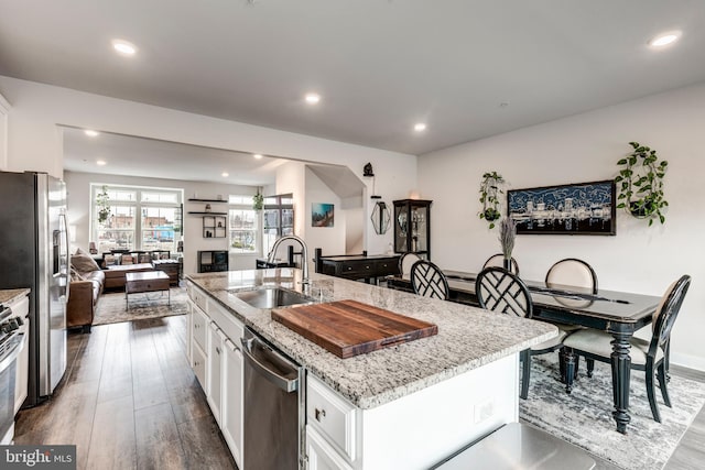 kitchen featuring dark wood-style floors, appliances with stainless steel finishes, white cabinets, a sink, and an island with sink