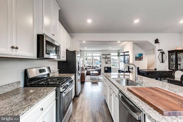 kitchen with white cabinets, appliances with stainless steel finishes, wood finished floors, light stone countertops, and a sink