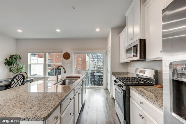 kitchen with an island with sink, appliances with stainless steel finishes, wood finished floors, white cabinetry, and a sink