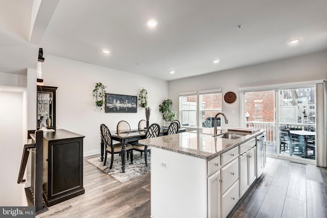 kitchen featuring a kitchen island with sink, wood finished floors, a sink, white cabinetry, and light stone countertops