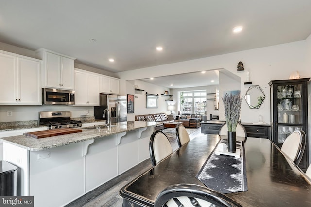 kitchen with recessed lighting, white cabinetry, open floor plan, appliances with stainless steel finishes, and light stone countertops