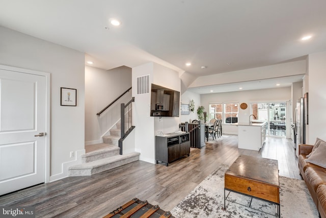 living area with light wood finished floors, recessed lighting, visible vents, stairway, and baseboards