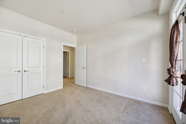 unfurnished bedroom featuring baseboards, a closet, and light colored carpet