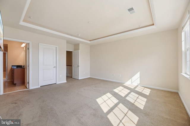 unfurnished bedroom with a tray ceiling, visible vents, and light carpet