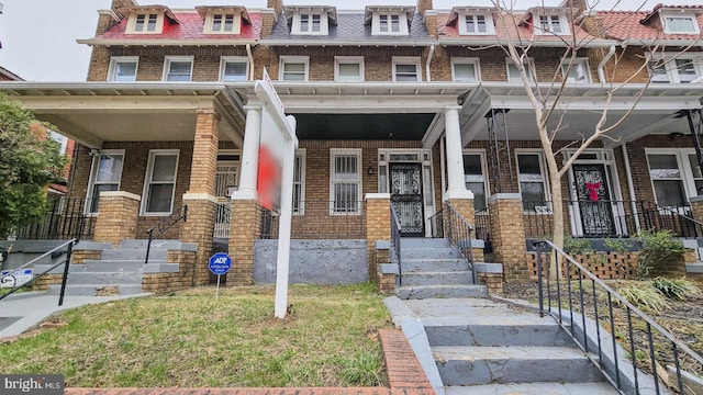 view of property with brick siding, covered porch, and mansard roof