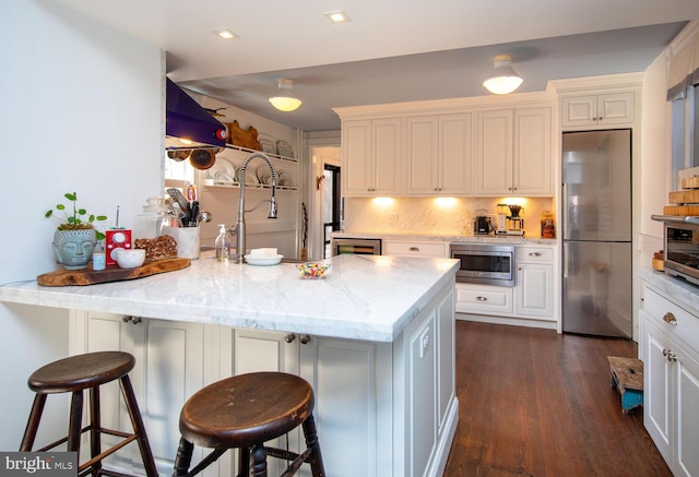 kitchen with a peninsula, a breakfast bar, appliances with stainless steel finishes, tasteful backsplash, and dark wood finished floors