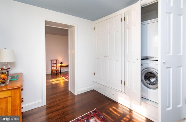 clothes washing area featuring dark wood-style floors, laundry area, stacked washer and dryer, and baseboards