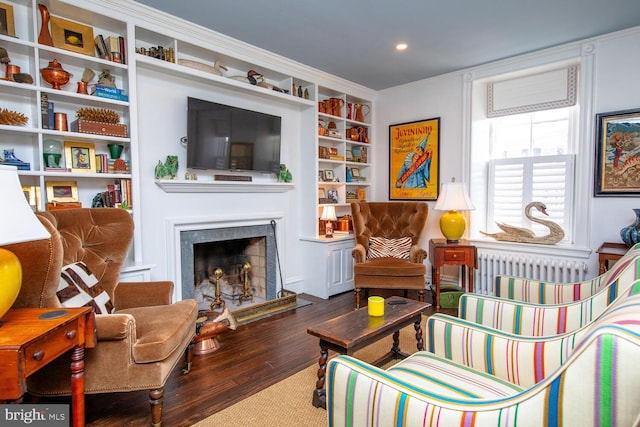 sitting room featuring built in features, a fireplace with raised hearth, radiator, ornamental molding, and wood finished floors