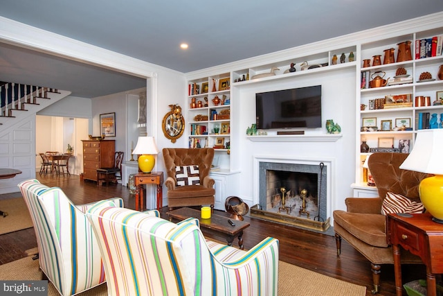 living area with built in features, crown molding, a fireplace, wood finished floors, and stairs