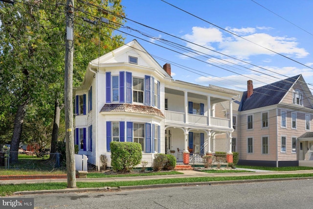 view of front facade with covered porch, a chimney, a balcony, and fence