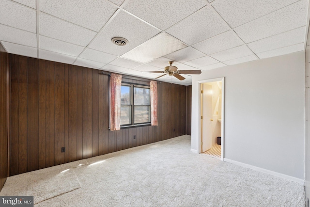 carpeted spare room with a ceiling fan, a drop ceiling, visible vents, and wooden walls