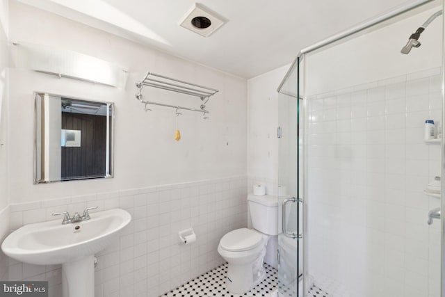 bathroom with a shower stall, a wainscoted wall, tile walls, and toilet