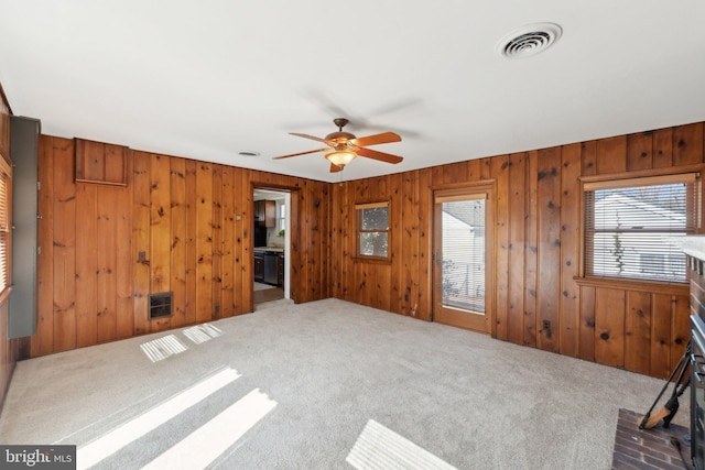 interior space with carpet floors, visible vents, ceiling fan, and wooden walls