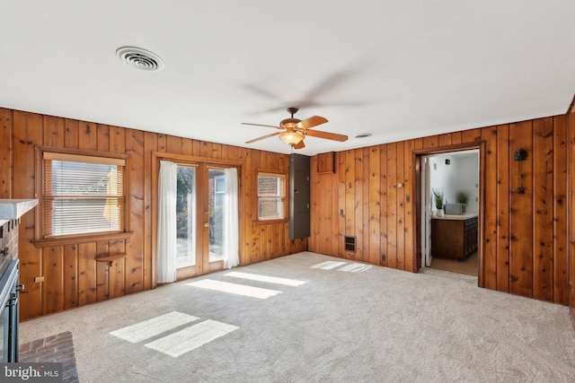 unfurnished living room featuring wood walls, carpet, visible vents, and a ceiling fan