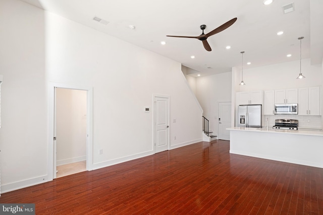 unfurnished living room featuring visible vents, a towering ceiling, a ceiling fan, wood finished floors, and stairs