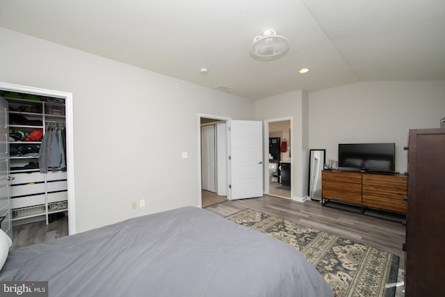 bedroom with a walk in closet, wood finished floors, recessed lighting, a closet, and lofted ceiling