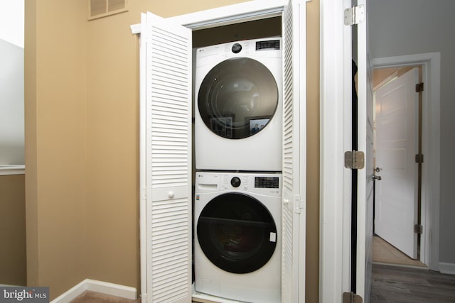 clothes washing area with laundry area, stacked washing maching and dryer, visible vents, and wood finished floors