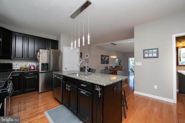 kitchen featuring light stone counters, light wood-style floors, appliances with stainless steel finishes, and a sink