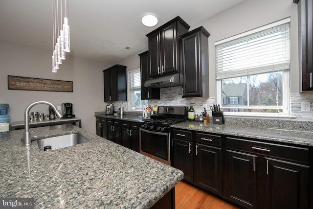 kitchen with stainless steel range with gas stovetop, a sink, under cabinet range hood, tasteful backsplash, and light wood-type flooring