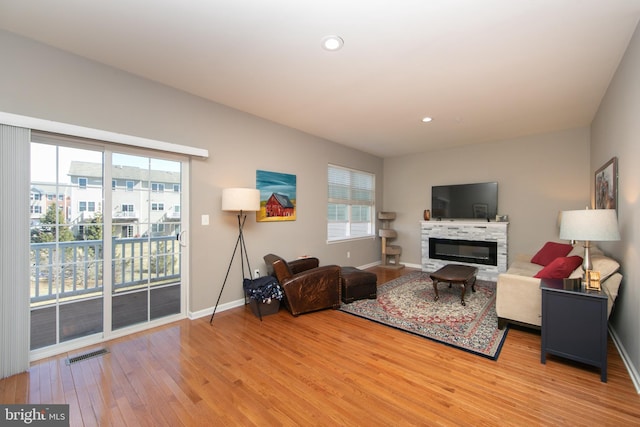 living room with visible vents, baseboards, light wood-type flooring, recessed lighting, and a glass covered fireplace